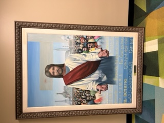 A painting of Jesus standing in the forefront with arms open. A group of people from various nations stand in the background. 