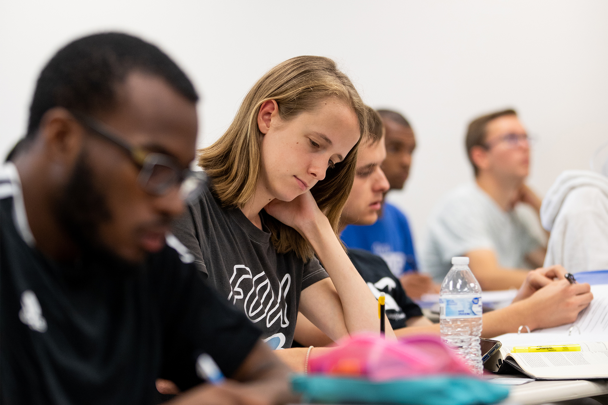 Five individuals are sitting behind a long table two are looking to the instructor, three are looking down taking notes. 